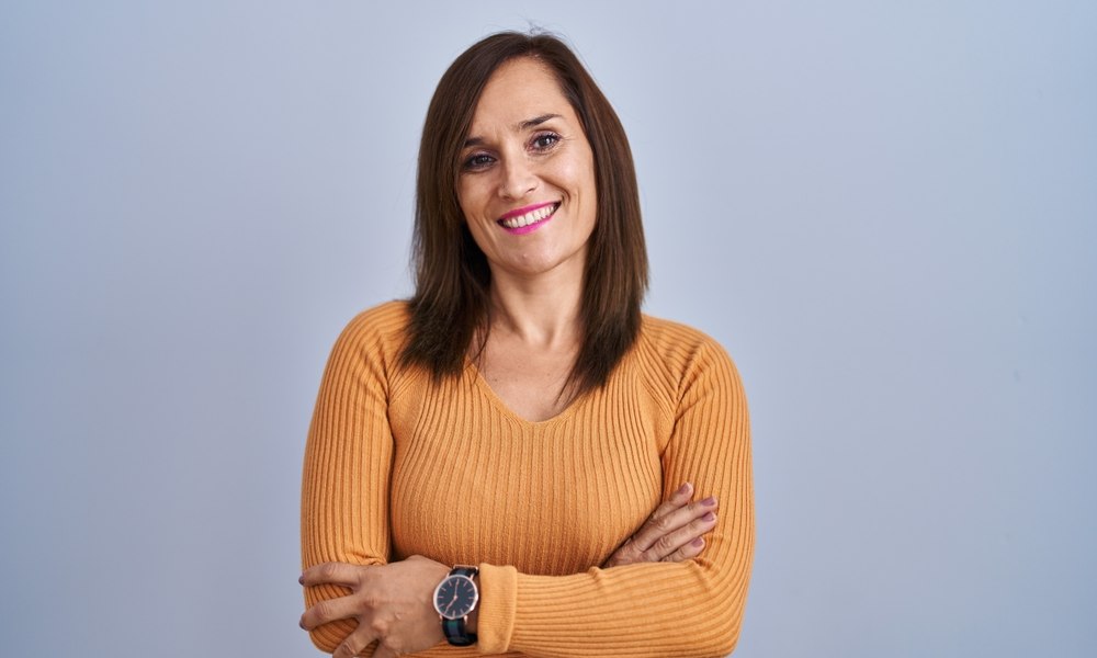 Une femme en gros plan, au centre de l'image, est entrain de sourire. Elle semble très heureuse car elle utilise la cryothérapie afin de combattre la ménopause et ses symptômes. Elle a un pull orange et le fond est bleu.