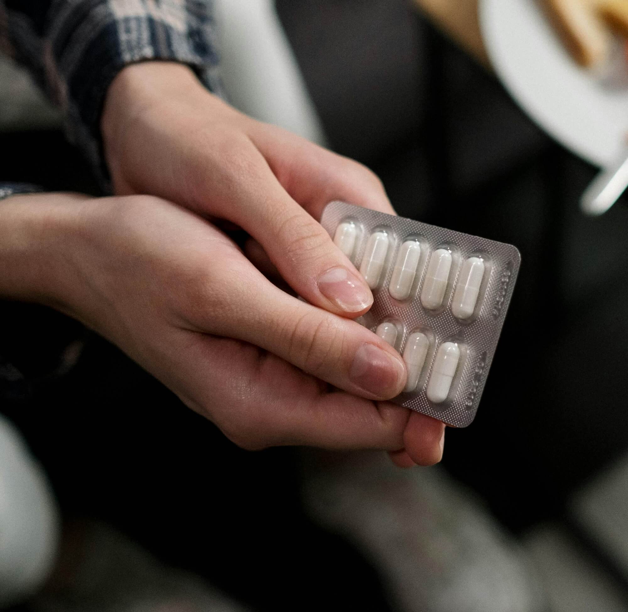 Une personne tient une plaquette de gélules blanches entre ses mains. L’image évoque les traitements hormonaux classiques, souvent utilisés contre les bouffées de chaleur.